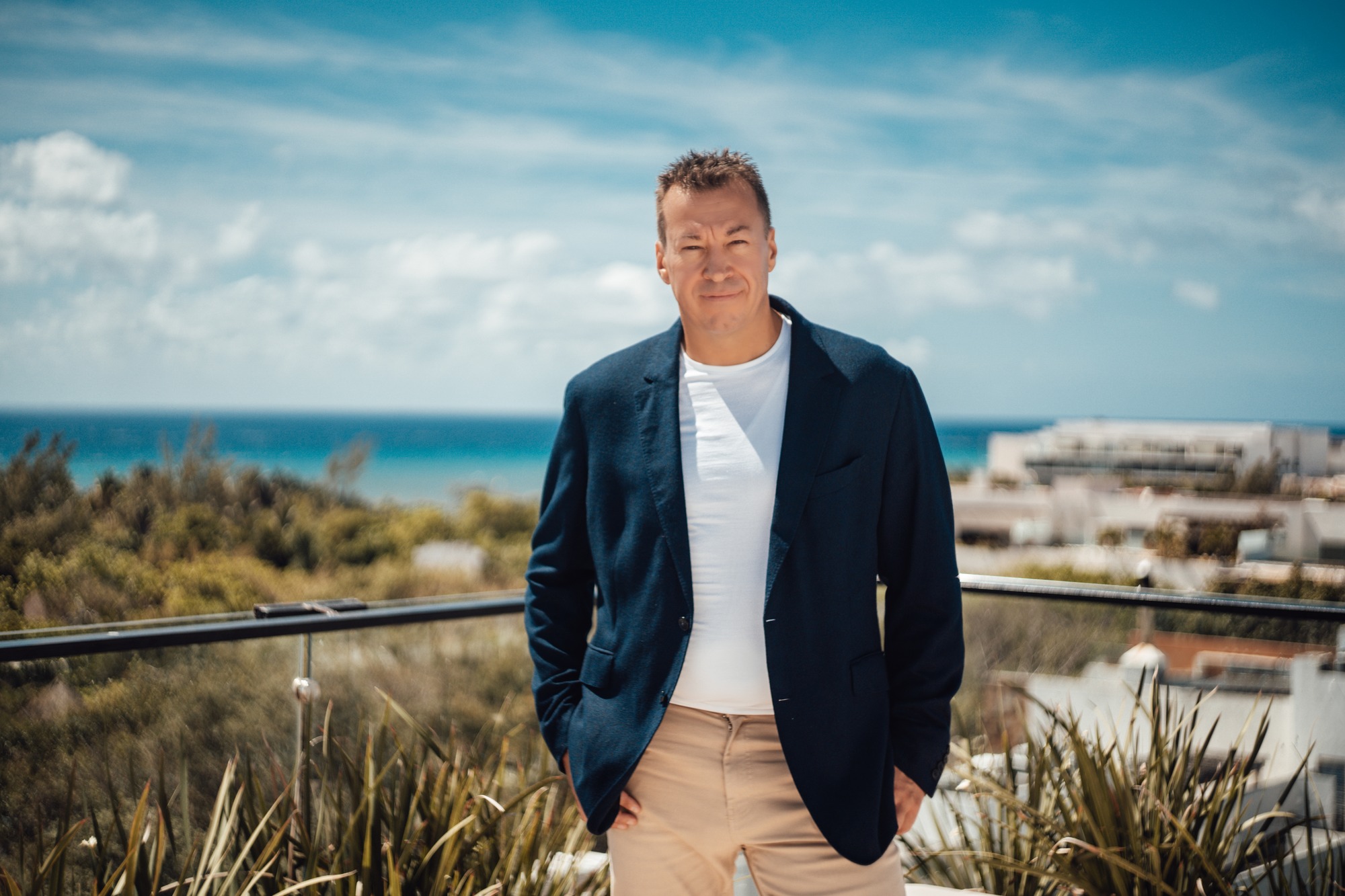 Man in a navy blazer on a coastal boardwalk, sea behind him