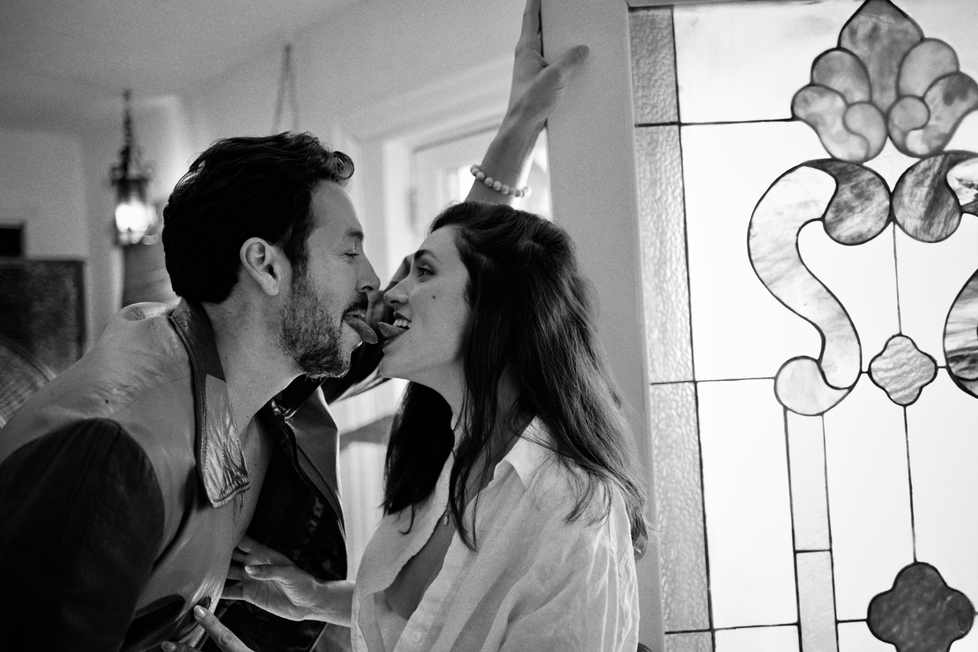 Black and white frame of a couple laughing close together beside a stained-glass window