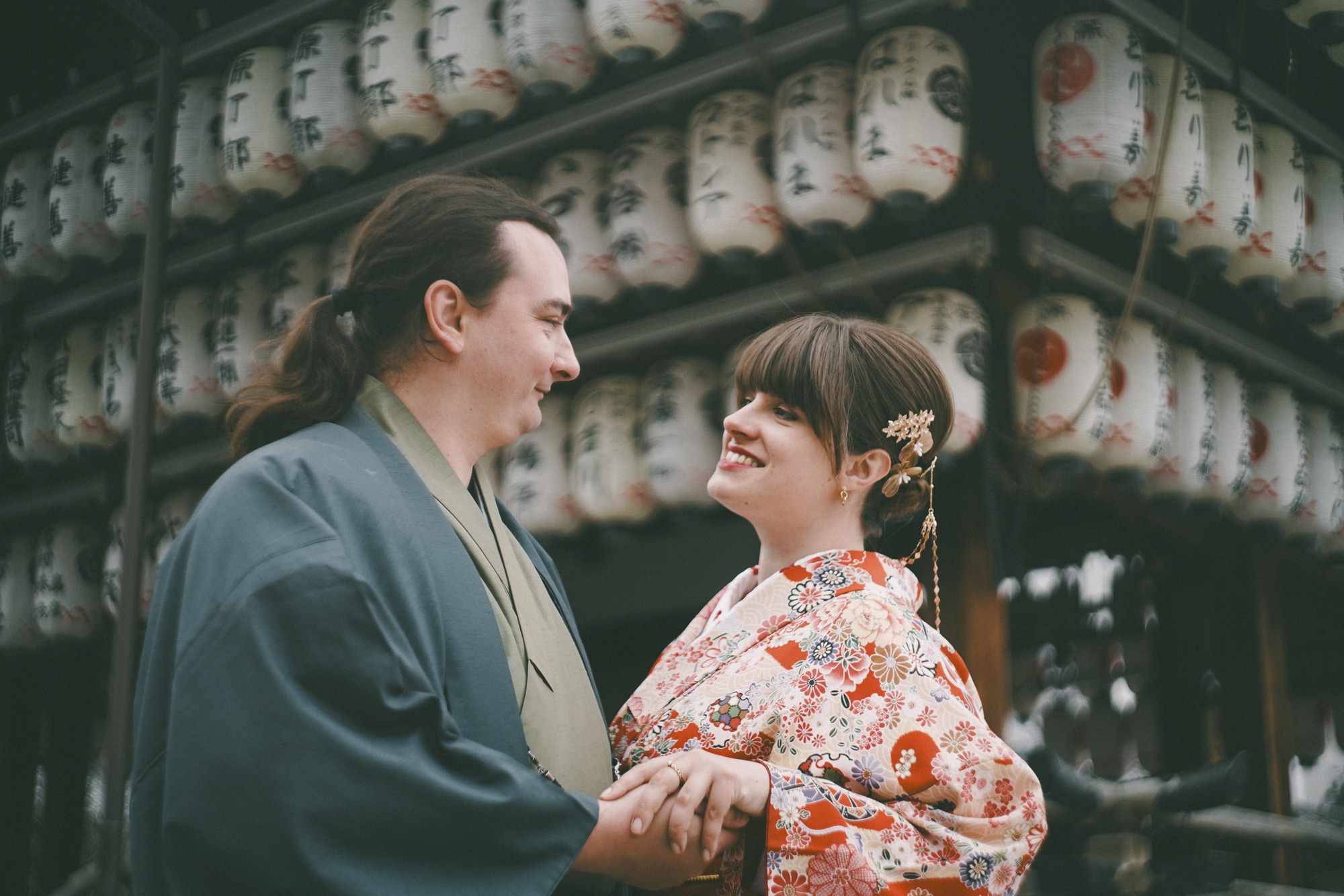 Couple in kimono holding hands beneath rows of paper lanterns