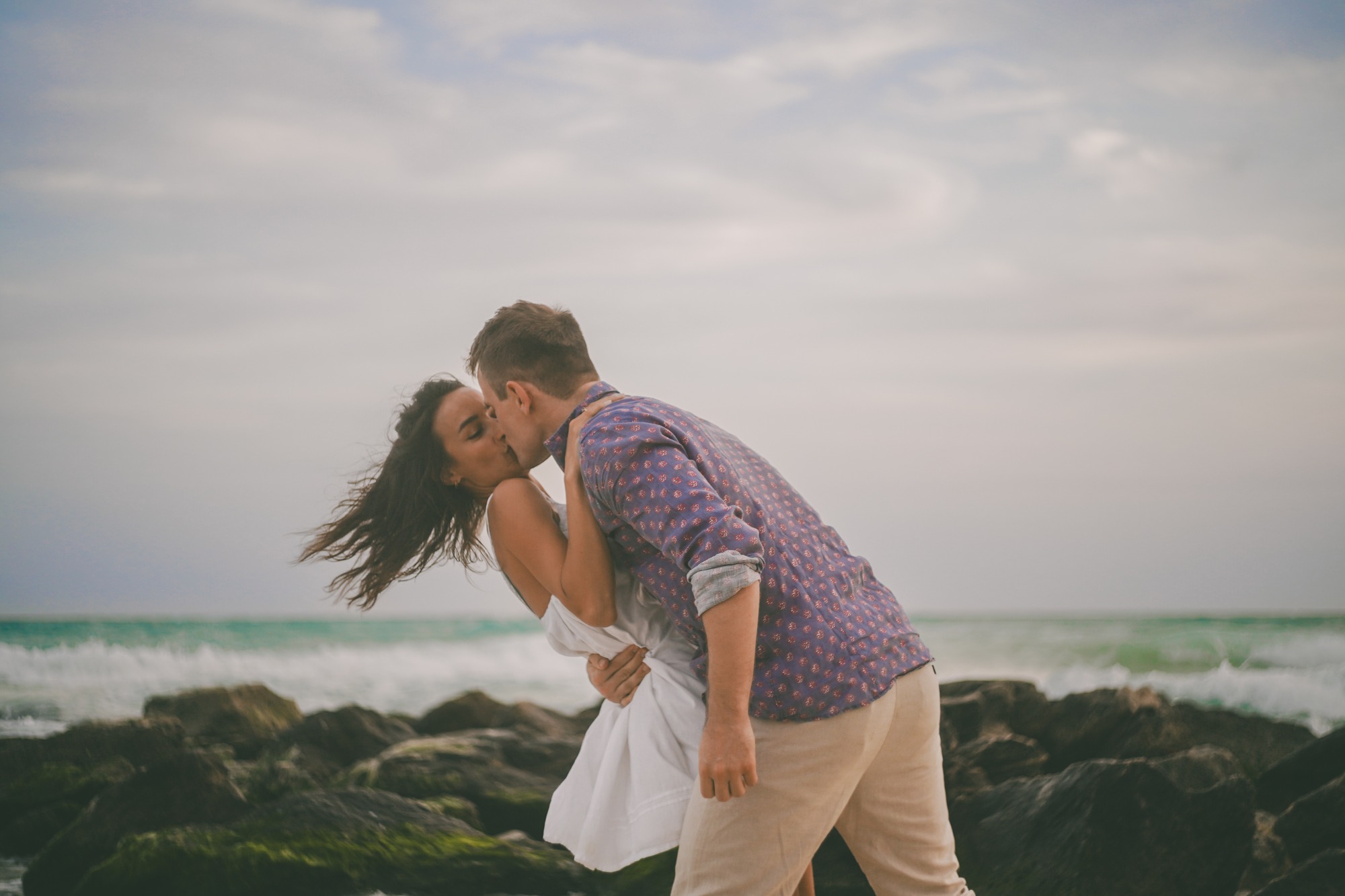 Couple kissing on the rocks by the sea, wind in her hair